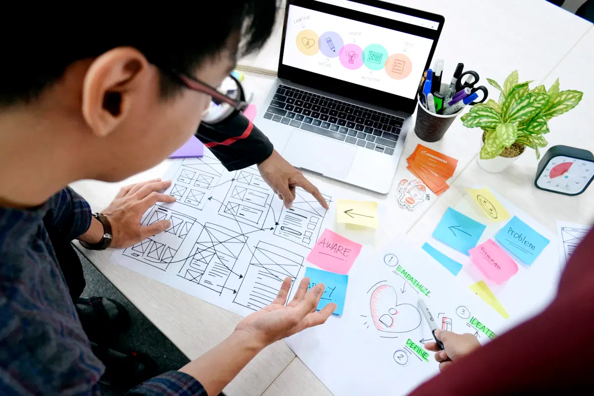 Web designers reviewing website wireframe sketches and sticky notes beside a laptop