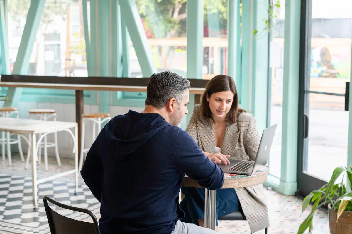 A business owner and a web designer meeting at a café table, looking at a laptop together