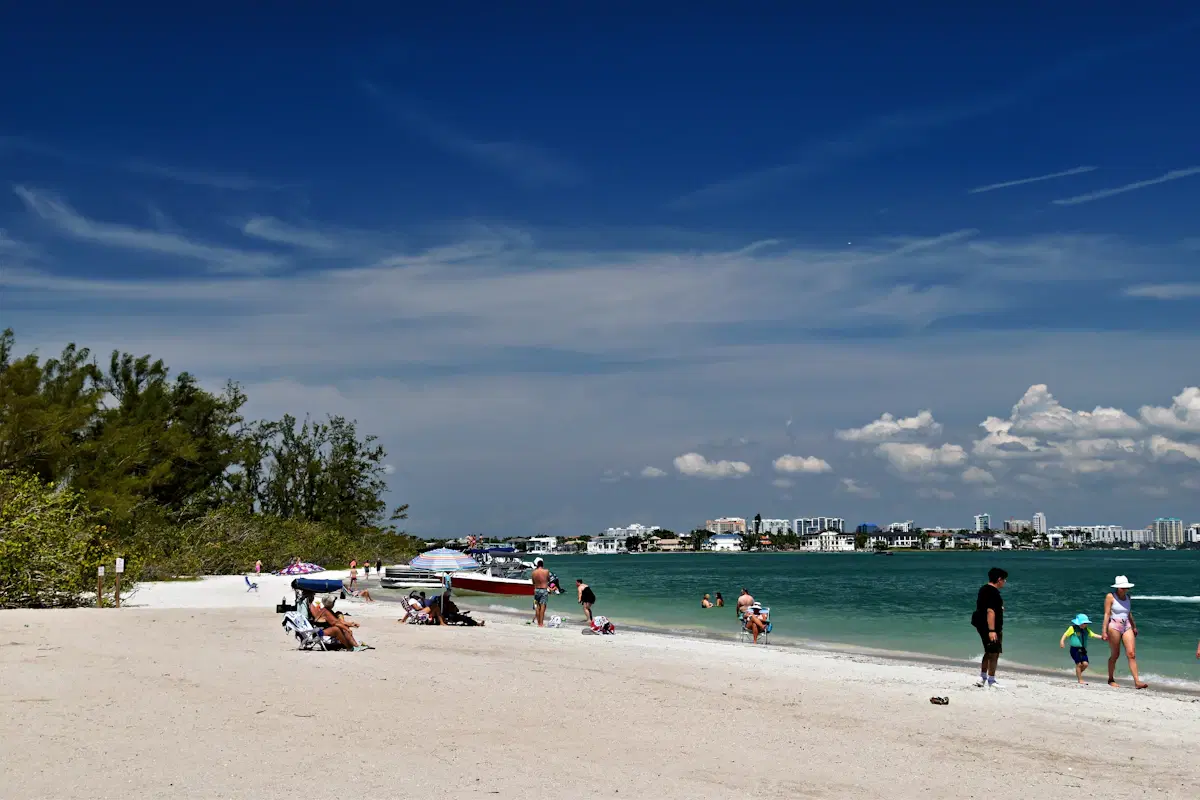 Beachgoers on the white sand at Lido Key Beach in Sarasota, with buildings across the water under a blue sky