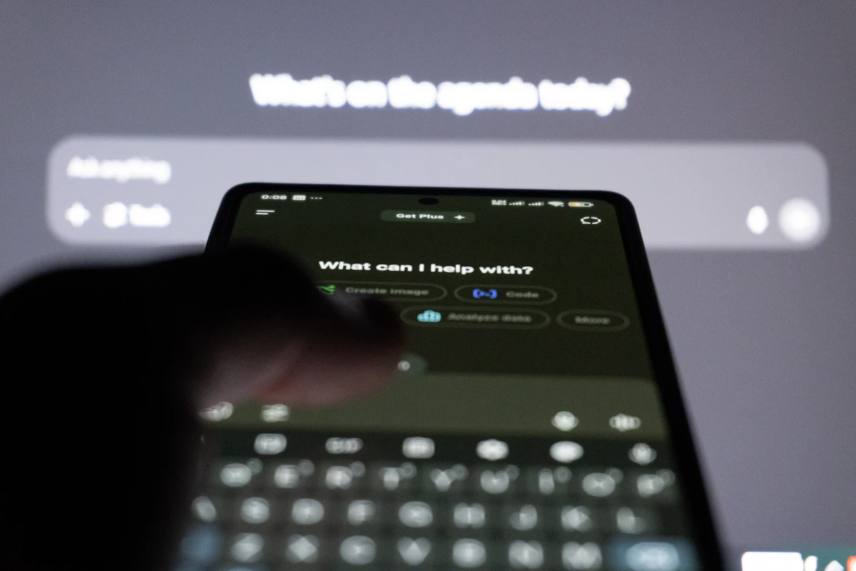Phone and screen showing an AI assistant prompt asking what it can help with