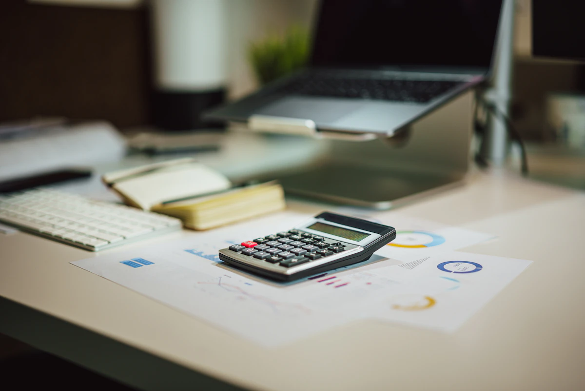 Calculator resting on printed charts beside a laptop on a desk, representing the full cost of a website quote